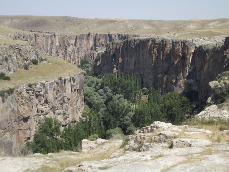 The steep rock walls of Ihlara Valley and the green valley floor below.
