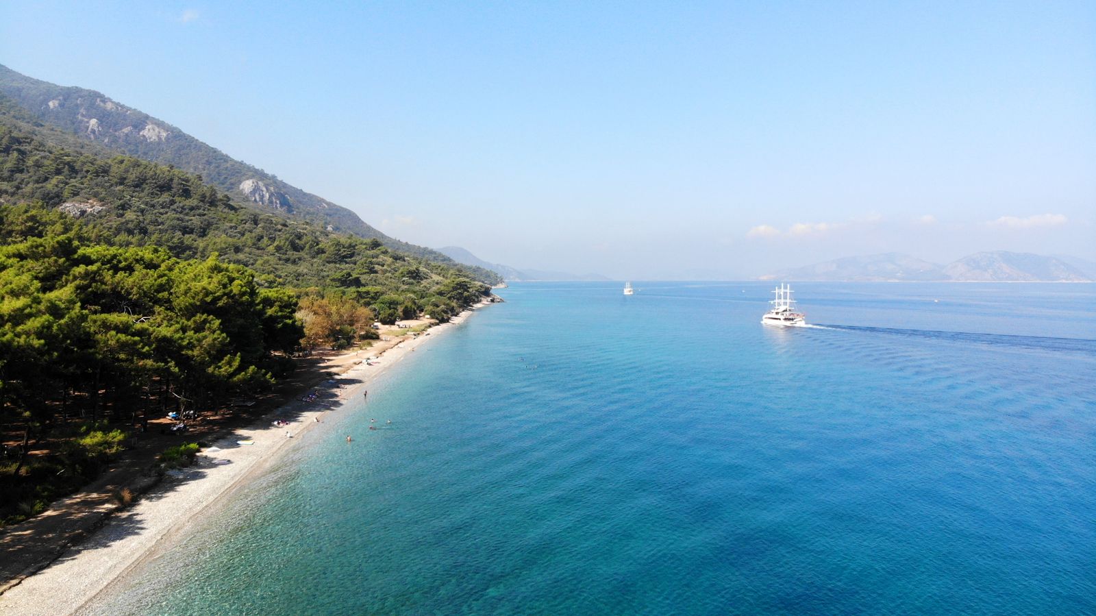 Pine forest running down to a pebble shore and turquoise water on the Dilek Peninsula.