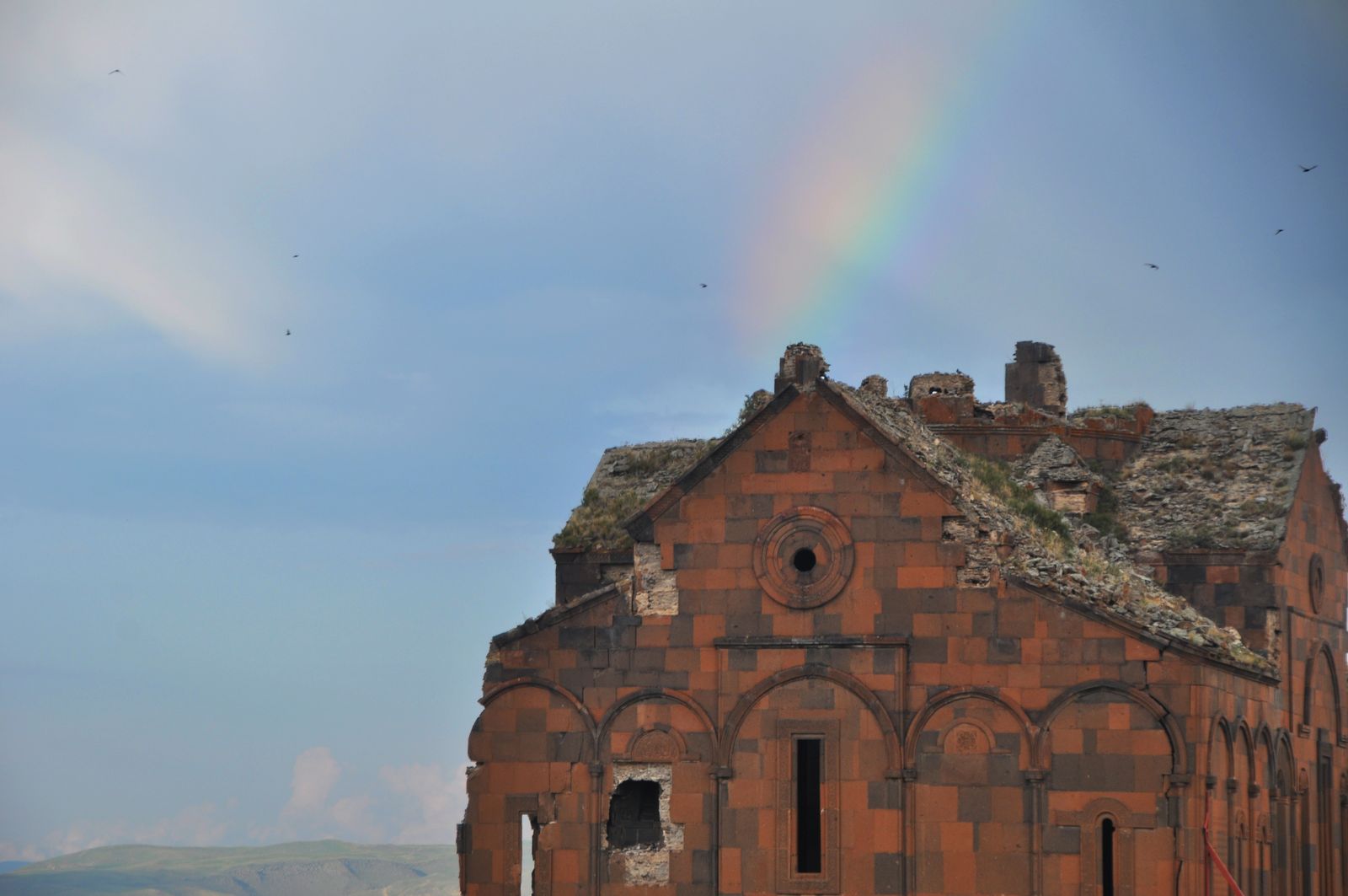 The red-stone facade of Ani Cathedral and surrounding ruins beneath a rainbow.